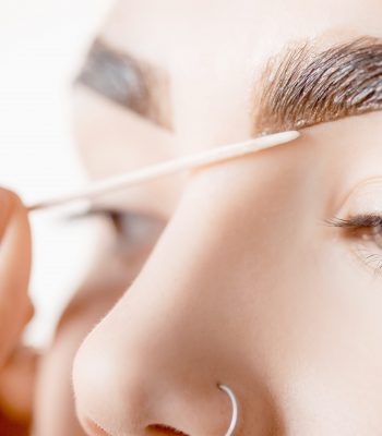 Correction and tint henna of eyebrows, master applies brush to woman marking on brow.